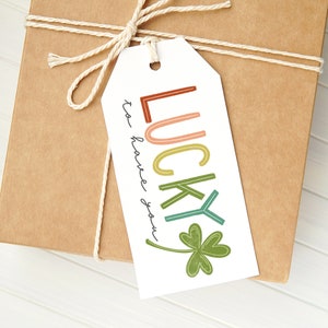 May include: A white gift tag with the text "Lucky to have you" in black cursive writing. The word "Lucky" is in colorful, outlined letters with a green four-leaf clover.
