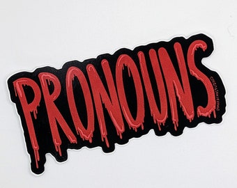 May include: A sticker with the word "PRONOUNS" in dripping red letters on a black background. The sticker has a white border and is on a white surface. The sticker is a statement piece.