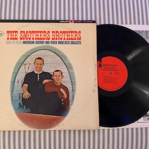May include: Vintage vinyl record album by The Smothers Brothers titled "American History and Other Unrelated Subjects." The album cover features a photo of the duo inside an oval frame. The record is black with a red label.