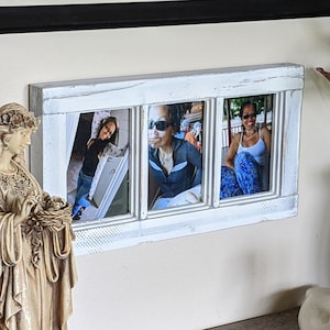 May include: A white wooden picture frame with three separate openings, each holding a black and white photograph of a person. The frame is mounted on a white wall. A white ceramic angel figurine is on the left side of the frame, and a white ceramic swan figurine is on the right side of the frame.
