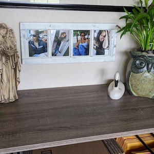 May include: A decorative scene featuring a beige angel statue, a white swan figurine, and a green owl-shaped planter holding a plant. A white framed photo display with four pictures hangs on the wall above the desk.