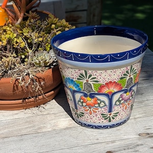 May include: A white ceramic planter with a blue rim and colourful floral designs. The planter has a traditional Mexican Talavera style.