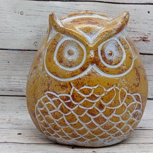Op de afbeelding: Een keramiek uilenbeeldje met een geel en wit verfdesign. De uil heeft een rond lichaam en grote ogen.