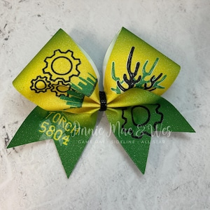 May include: Green and yellow cheer bow with black and white gear designs and the text "Torch 5804 Annie Mae & Wes Game Day Sideline Allstar".