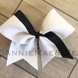 Op de afbeelding: Een witte cheer bow met een zwarte glitterstreep. De strik is vastgebonden met een zwart lint.