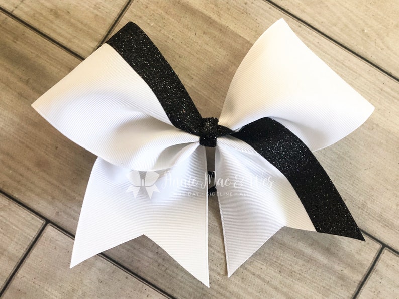 Op de afbeelding: Een witte cheer bow met een zwarte glitterstreep in het midden.