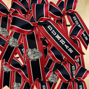 May include: A group of red and black striped hair bows with a bulldog logo and the text "Dunbar" printed on them.