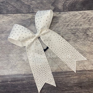 May include: A white cheer bow with silver rhinestones. The bow is tied with a black elastic band.