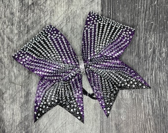 May include: A large purple and black cheer bow with silver glitter and rhinestones. The bow is tied in a classic cheer bow shape.