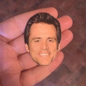 May include: A close-up of a paper cutout of a man's face. The man has short brown hair, brown eyes, and a light complexion. He is smiling with his teeth showing.