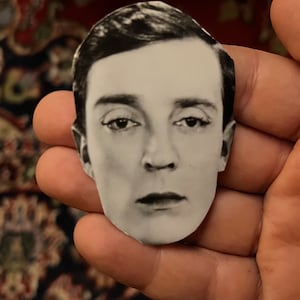 Puede incluir: Fotografía en blanco y negro de la cara de un hombre. La foto está recortada y se sostiene en la mano de alguien.