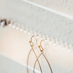 Close up showing how to hang both studs and dangling earrings on the unique and beautiful modern clear acrylic earring storage piece