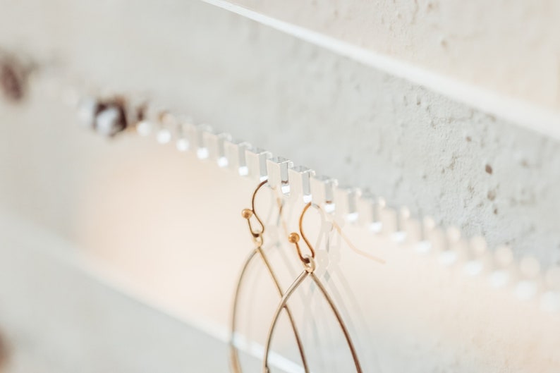 Close up showing how to hang both studs and dangling earrings on the unique and beautiful modern clear acrylic earring storage piece