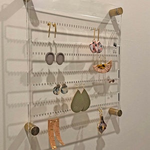 Both studs and dangling earrings hanging on the unique and beautiful modern clear acrylic earring storage piece with gold hardware