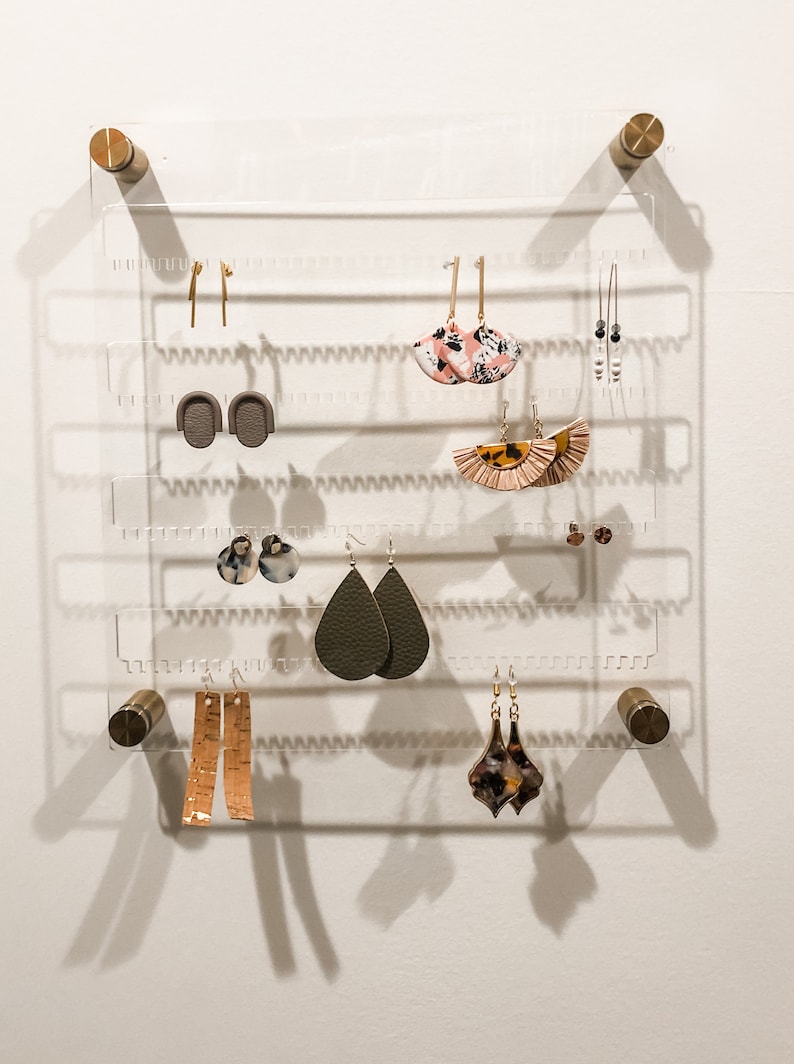 Both studs and dangling earrings hanging on the unique and beautiful modern clear acrylic earring storage piece with gold hardware