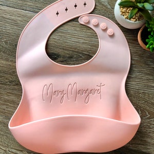 Custom Pink Baby Bib with Baby's name laser engraved onto center on wooden background