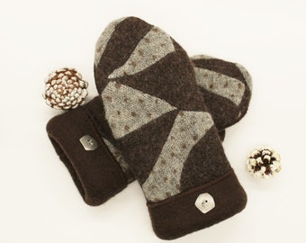 May include: A pair of dark brown and light gray knit mittens featuring a geometric triangular pattern with small brown dots. Each mitten has a solid dark brown cuff accented with a single silver-toned button. Two small pinecones are visible.