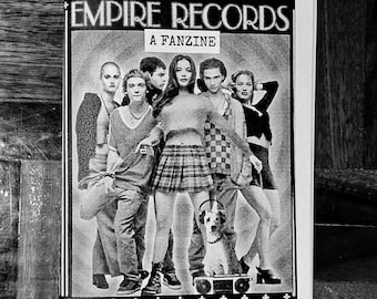May include: Black and white zine cover featuring the text "EMPIRE RECORDS" and "A FANZINE". The cover art depicts a group of people, with a dog wearing headphones on a boombox. The zine is on a wooden surface.