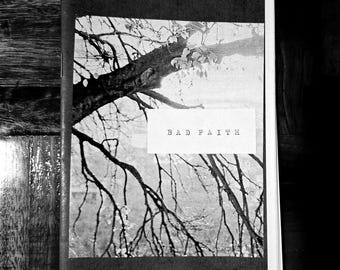 May include: Black and white zine with a tree branch and leaf image on the cover. The text "BAD FAITH" is printed in a rectangular box. The zine is open on a wooden surface.