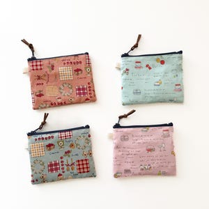May include: Four small, square fabric pouches with zipper closures and brown leatherette pulls. Each pouch features a unique pattern with kitchen-themed illustrations, including cherries, wreaths, and checkered designs. The pouches are in shades of pink and blue.
