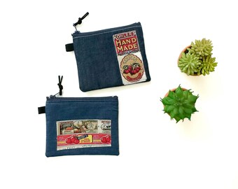 May include: Two denim zipper pouches with vintage-style cherry label patches. One pouch features a "Kohler's Hand Made" label. The other has a label with the text "Best's Cherries". Small black zipper pulls and a black fabric loop are attached.