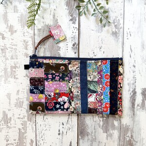May include: A patchwork fabric zippered pouch with a variety of floral and geometric patterns in shades of pink, red, blue, green, and brown. The pouch has a denim strip down the center and a black zipper.