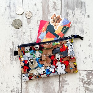 May include: A small zippered pouch with a colorful print of cartoon dogs. The pouch is open and a gift card with the text "Happy Birthday" is partially visible inside.