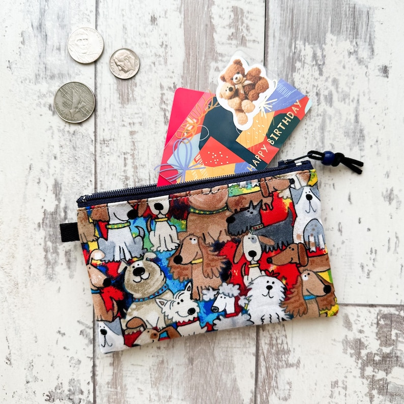 May include: A small zippered pouch with a colorful print of cartoon dogs. The pouch is open and a gift card with the text "Happy Birthday" is partially visible inside.