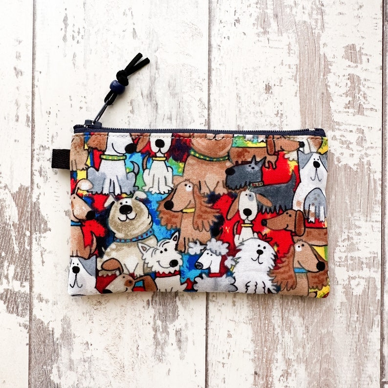 May include: A zippered pouch with a colorful print of cartoon dogs. The pouch is made of fabric and has a black zipper.