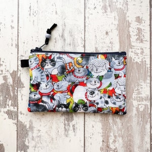 May include: A zippered pouch with a colorful print of cats. The pouch is made of fabric and has a black zipper.