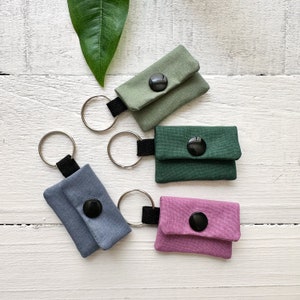 May include: Four keychains with small fabric pouches and black buttons. The pouches are in shades of green, blue, and pink.
