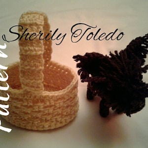 May include: A crocheted basket with a handle, in a cream color, next to a brown crocheted animal. The text "Sherily Toledo Pattern" is written in black cursive on the left side of the image.