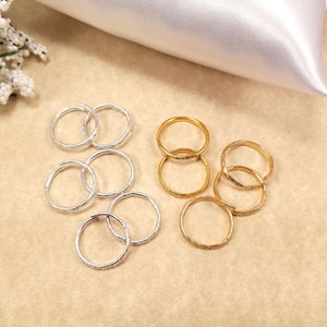 Multiple inexpensive gold and silver rings displayed on a table with a wedding theme. They are used to replace real wedding bands on a ring pillow during the ceremony.