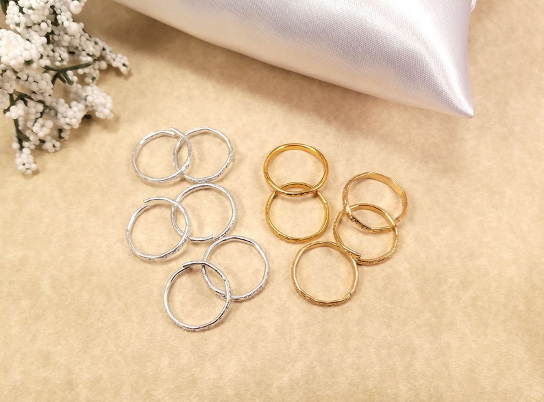 Multiple inexpensive gold and silver rings displayed on a table with a wedding theme. They are used to replace real wedding bands on a ring pillow during the ceremony.