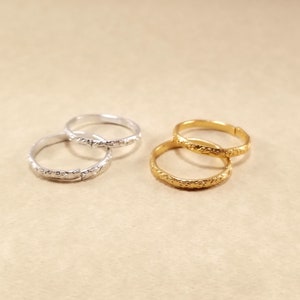 Close view of inexpensive gold and silver rings displayed on a beige table. Rings have designs around the edges.