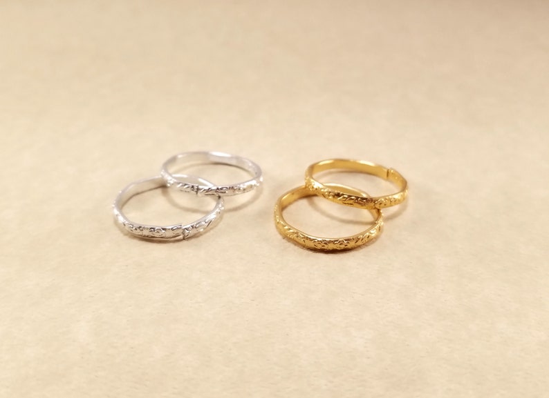 Close view of inexpensive gold and silver rings displayed on a beige table. Rings have designs around the edges.