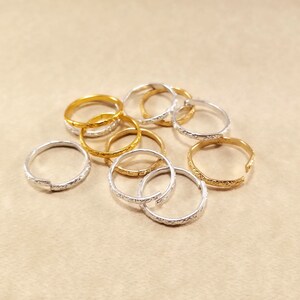 Close view of several inexpensive gold and silver rings displayed on a beige table. Rings are bent to an open position to show they are adjustable.