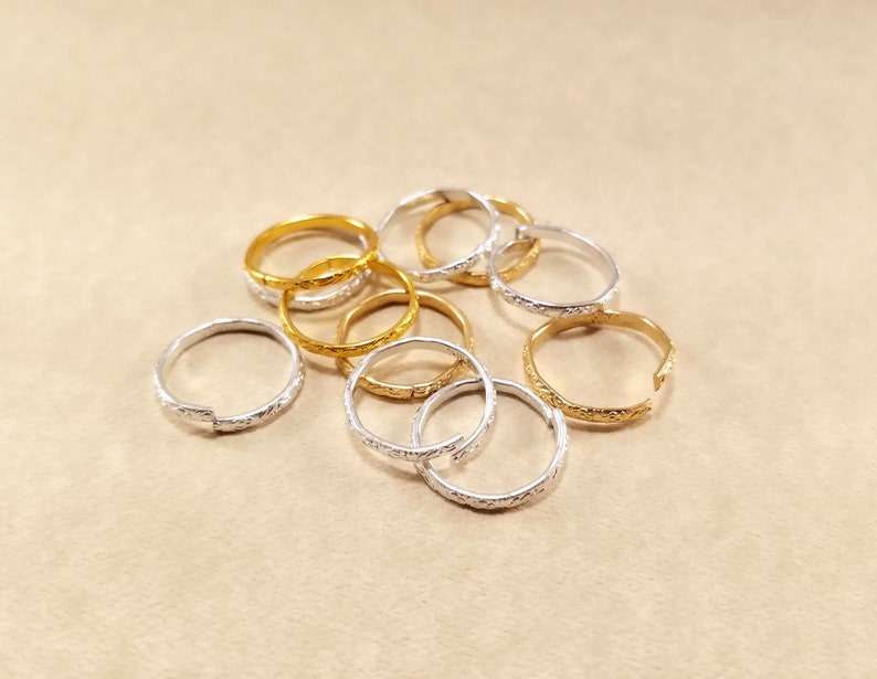 Close view of several inexpensive gold and silver rings displayed on a beige table. Rings are bent to an open position to show they are adjustable.