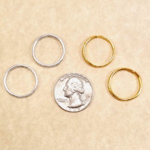 Four imitation gold and silver rings surrounding a US quarter for size comparison. Shows that the rings are slightly smaller than the coin.