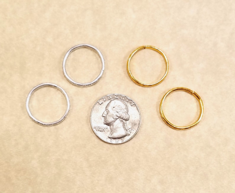 Four imitation gold and silver rings surrounding a US quarter for size comparison. Shows that the rings are slightly smaller than the coin.