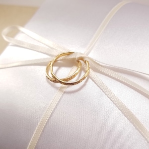 Close photo of imitation gold rings tied to the center of a white ring bearer pillow. Details of a floral design around the edge of the rings is visible.