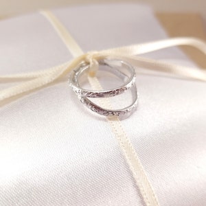 Close photo of imitation silver rings tied to the center of a white ring bearer pillow. Details of a floral design around the edge of the rings is visible.