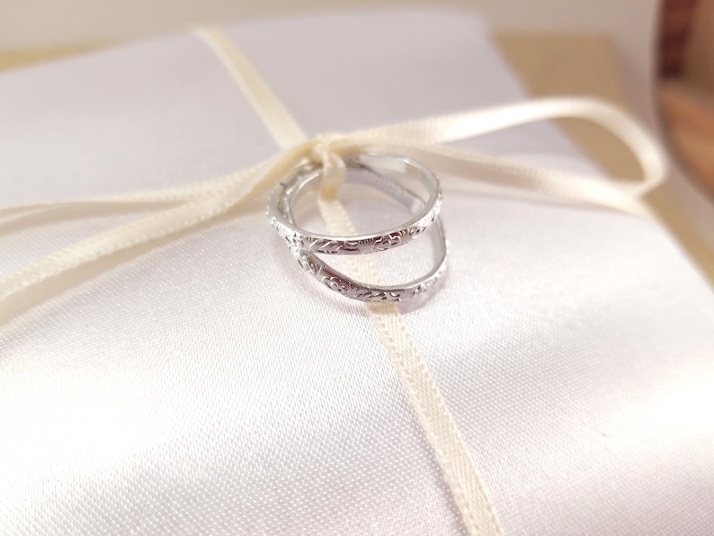 Close photo of imitation silver rings tied to the center of a white ring bearer pillow. Details of a floral design around the edge of the rings is visible.