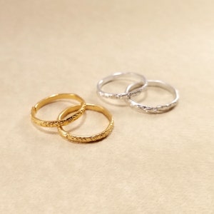 Close view of inexpensive gold and silver rings displayed on a beige table. Rings have designs around the edges.