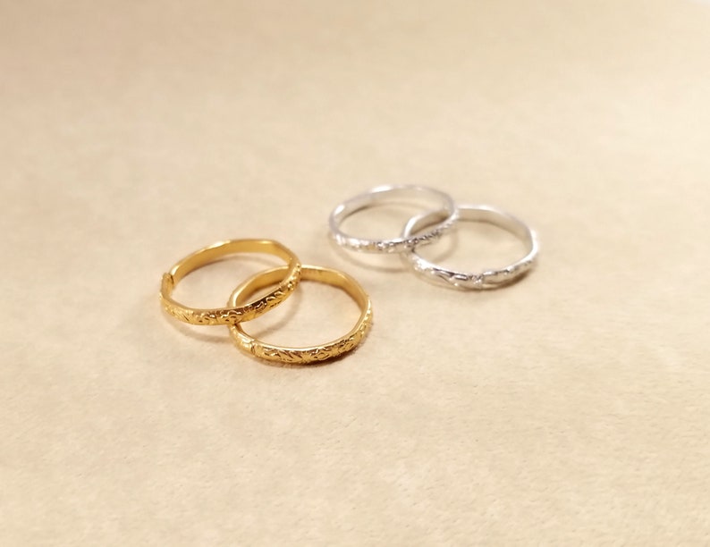 Close view of inexpensive gold and silver rings displayed on a beige table. Rings have designs around the edges.