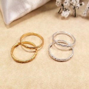 Four inexpensive gold and silver adjustable rings displayed on a beige table with wedding pillow and flowers. They are used to replace real wedding bands on a ring pillow during the ceremony.