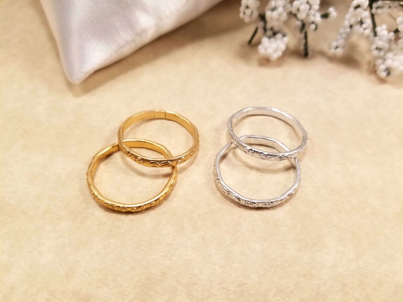 Four inexpensive gold and silver adjustable rings displayed on a beige table with wedding pillow and flowers. They are used to replace real wedding bands on a ring pillow during the ceremony.