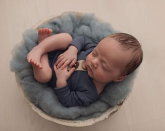 Könnte beinhalten: Ein neugeborenes Baby schläft friedlich in einer blauen und weißen Schüssel, trägt einen blauen langärmeligen Strampler mit einem braunen Knopf.