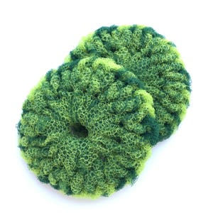 May include: Two green and yellow scrubbers made of a mesh material. The scrubbers are round and have a hole in the center.