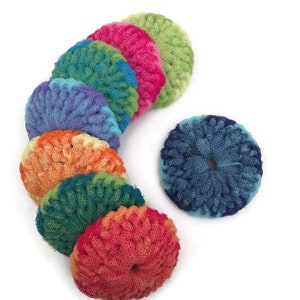 May include: A set of eight colorful crocheted scrubbers in a rainbow of colors, including red, orange, yellow, green, blue, purple, and pink. The scrubbers are round and have a hole in the center.